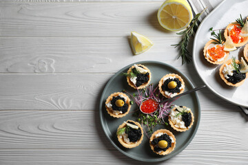 Delicious tartlets with red and black caviar served on white wooden table, flat lay. Space for text