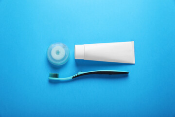 Container with dental floss, toothpaste and toothbrush on light blue background, flat lay