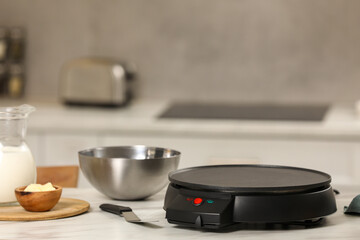 Electrical crepe maker and ingredients on white marble table in kitchen, space for text
