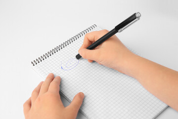 Child erasing doodle drawn with erasable pen in notepad against white background, closeup