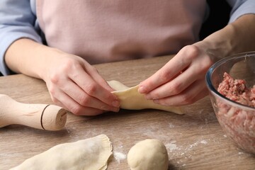 Woman making chebureki at wooden table, closeup