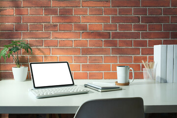 Stylish workspace with digital tablet, books, coffee cup and houseplant on white desk.