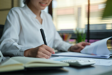 A young female administrative assistant making notes of working planning organizing information in her office.