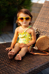 Adorable toddler baby girl wearing fashionable sunglasses and yellow swimsuit sitting on beach...