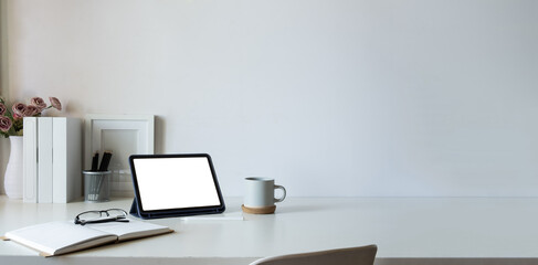 Minimal workplace with digital tablet, cup of coffee and houseplant on white table. Copy space for text.