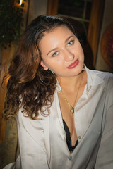 Portrait of a beautiful girl with curly hair in a white dress and black leather shorts sitting on a bar stool. Latina girl with beautiful green eyes