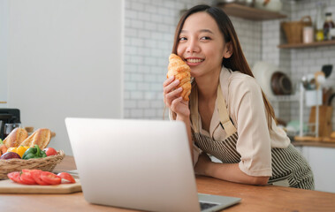 Photo of cheerful woman eating croissant while having breakfast in modern kitchen.