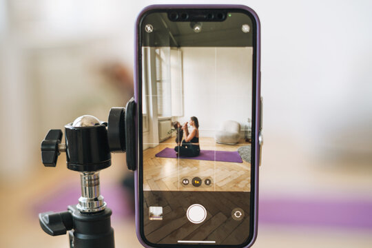 Young woman with little daughter fitness blogger doing exercises and recording video on mobile phone in studio - Powered by Adobe