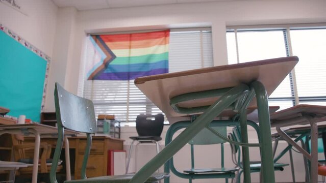 A desk in a classroom with a pride flag on the wall of school learning