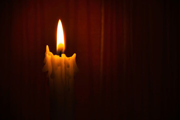 Single yellow wax candle burning alone in the dark red