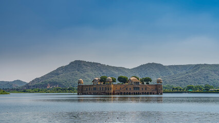 The mysterious Jal Mahal is a palace in the middle of the artificial Man Sagar Lake. Above the water is the top floor of a flooded building with arches, domes, green trees in a roof garden. India.