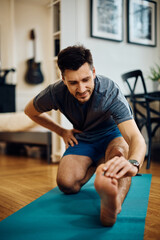 Athletic man doing stretching exercises while warming up for home workout.