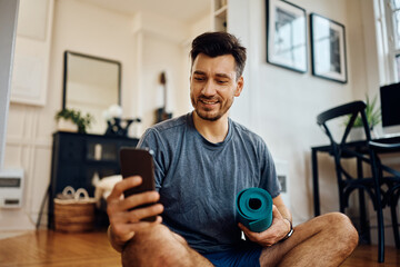 Happy athlete using mobile phone while working out at home.