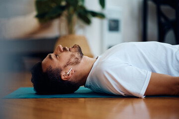 Male athlete listening music over earbuds while resting on floor after home workout.