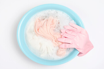 Wash basin with clothes and rubber gloves on white background close-up, top view.