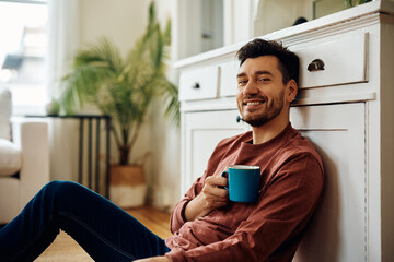 Happy man enjoying in cup of coffee at home and looking at camera.