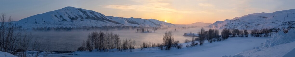Panoramic winter view of the mountains in the snow and at sunset the river in the fog