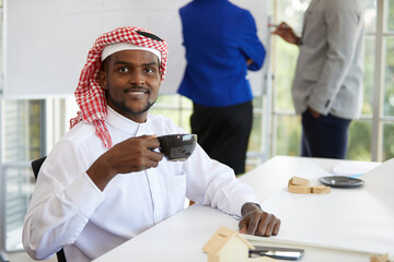 young African muslim businessman in white traditional outfit, holding a cup of coffee in the office