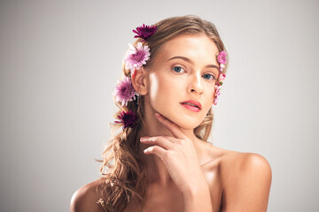 Naklejka premium Portrait, skincare and woman with flowers, cosmetics and dermatology with lady on grey studio background. Face, female and lady with plants, florals in hair or makeup with grooming or morning routine