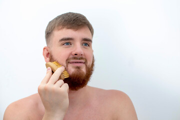 Handsome young bearded guy, European brutal man with a beard hair is combing the beard on face with...
