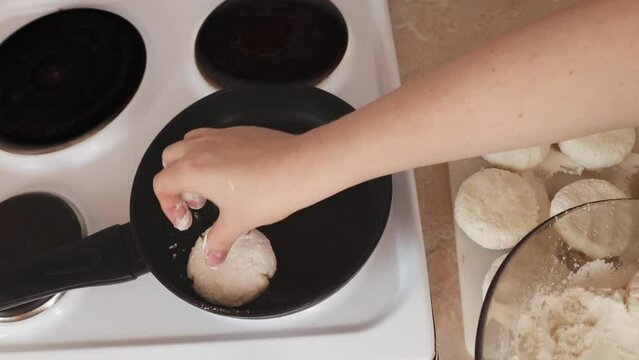 Women's hands put cottage cheese pies on a hot pan. Cheesecakes are fried in a pan. The process of preparing delicious homemade food. cheesecakes or cheesecakes. close-up. Cottage cheese balls, health