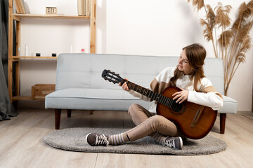 Photo of a young woman playing the guitar sitting in the living room. Girl singing a new song...
