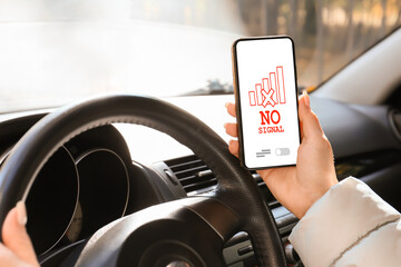Woman holding mobile phone with text NO SIGNAL on screen while driving car