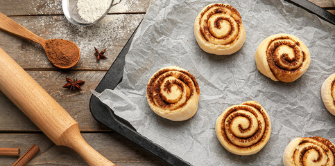 Baking tray with uncooked cinnamon rolls on wooden background