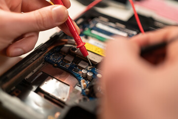 Fototapeta na wymiar Close up of male hands testing laptop motherboard using multimeter.
