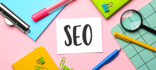 Paper sheet with abbreviation SEO and stationery on pink background