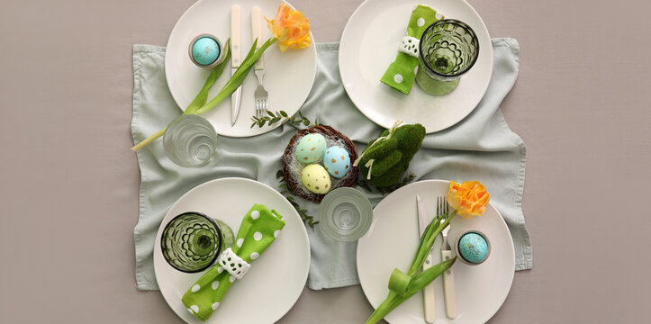Beautiful table setting with Easter eggs and floral decor on grey background