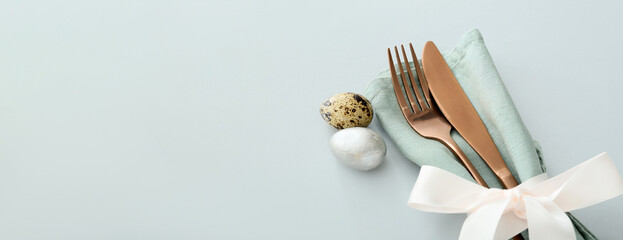 Cutlery with napkin and Easter eggs on grey background with space for text