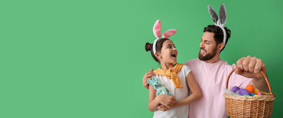 Little girl and her father with Easter eggs and bunny ears on green background with space for text