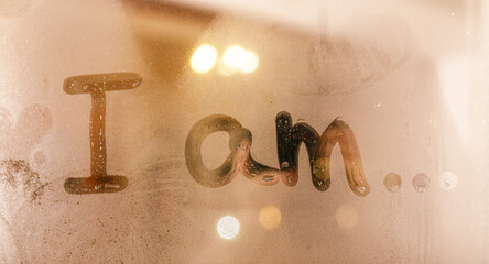 The inscription I am.. written on a window flooded with raindrops on a blurred glassy background in the city
