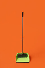 Plastic dustpan with cleaning broom on color background