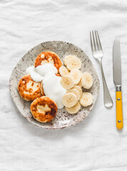 Cottage cheese syrnyky with greek yogurt and banana on a light background, top view