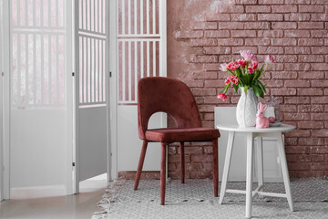 Vase with tulips and Easter bunny on end table and armchair near brick wall