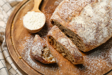 Board with sliced loaf of rye bread and spoon of flour on napkin