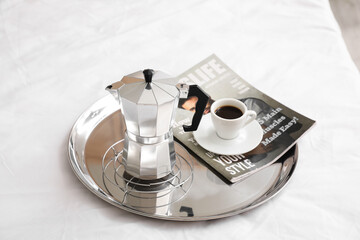 Tray with geyser coffee maker, cup of espresso and magazine on bed