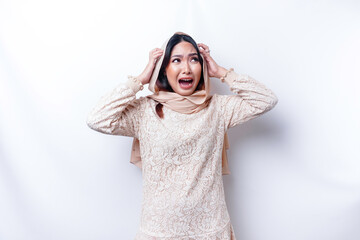 A dissatisfied young Asian Muslim woman looks at the camera posing on a white background,...