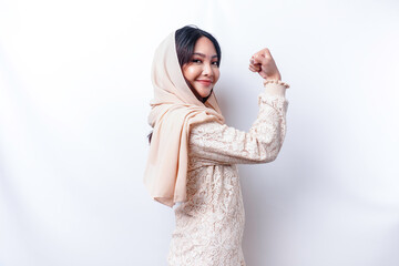 Excited Asian Muslim woman wearing a hijab showing strong gesture by lifting her arms and muscles...