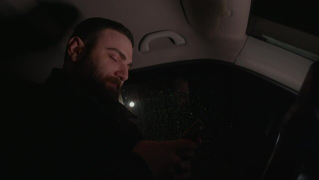 Handsome young man forgets about the busy day while texting in the car's front seat