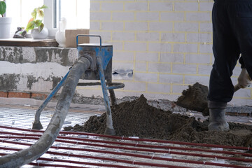 Semi-dry floor screed - a worker shovels a construction mixture through a special sleeve for...