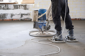 Ramming and grinding of semi-dry floor screed by a machine with a rotating disk for leveling. Construction of a concrete floor in the house, a master with special equipment.