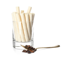 Glass with delicious wafer rolls  and spoon of coffee beans isolated on white background