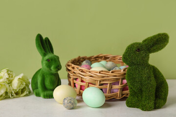 Easter bunnies and wicker basket with painted eggs on table against green background