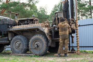 Obraz premium Team of workers with drilling rig on car are drilling artesian well for water in ground. Insertion of metal casing pipe into ground, installation of individual drinking supply, June 28, 2022, Russia,