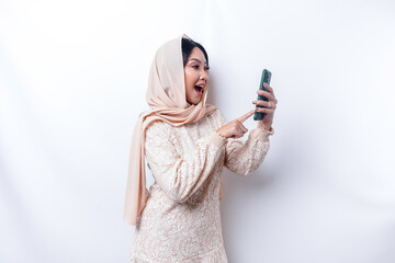 A portrait of a happy Asian Muslim woman wearing a hijab, holding her phone, isolated by white background