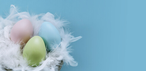 Easter eggs in a nest with feathers, turquoise Easter background. Vertical photo.