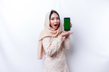 Shocked Asian woman wearing hijab, showing copy space on her phone screen, isolated by white background
